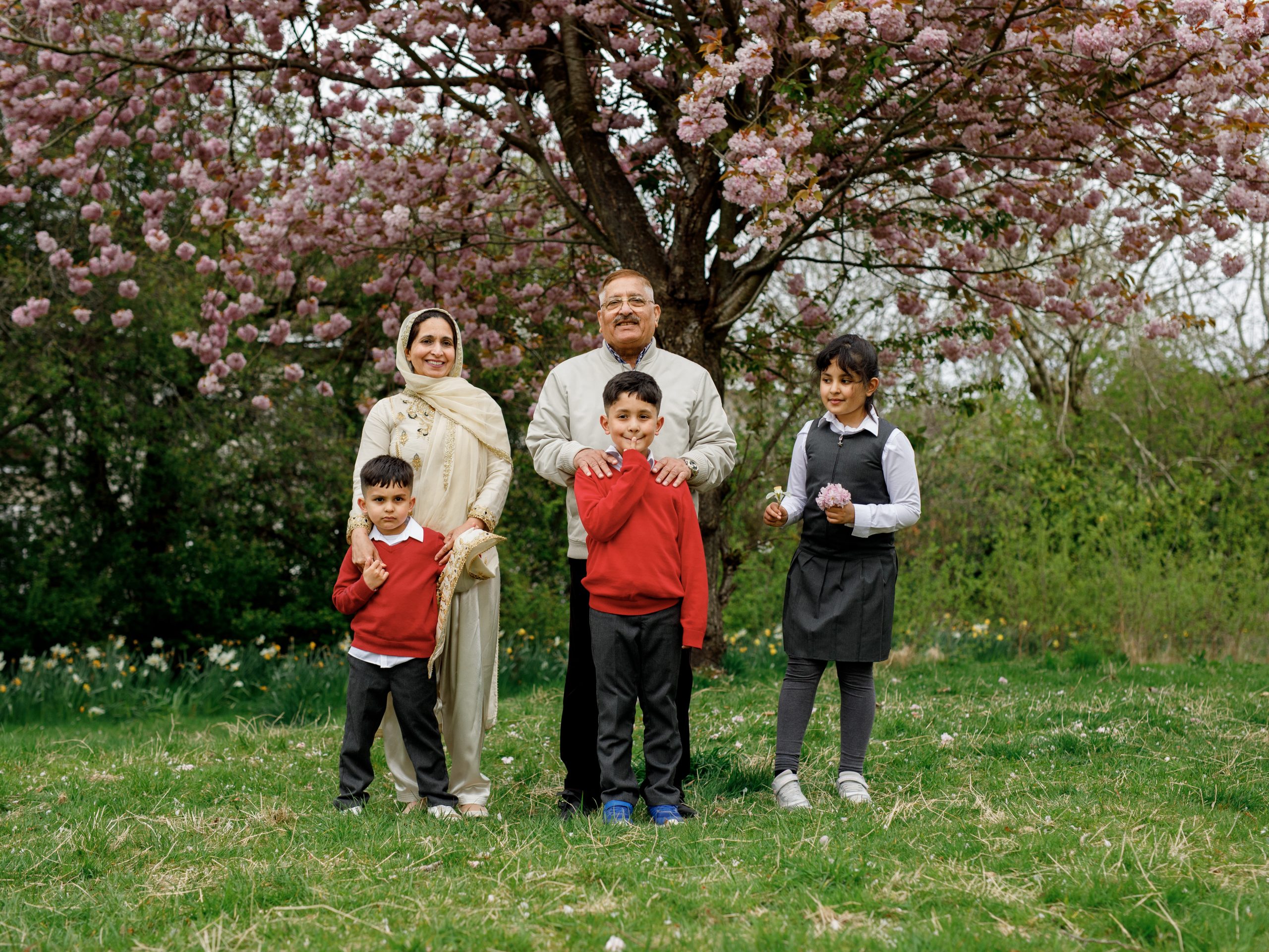 Family posing happily under blooming cherry blossom tree in a lush green park.