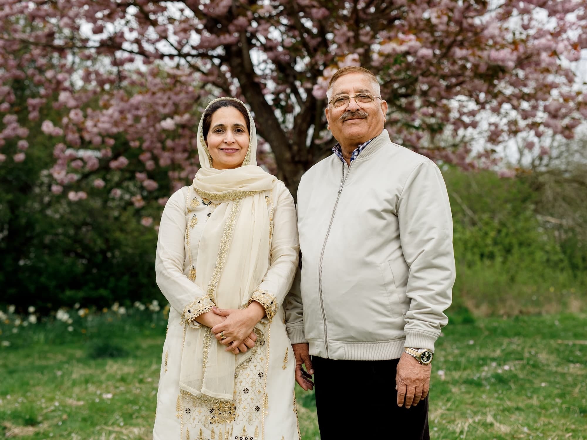 Couple smiling under a blooming cherry blossom tree in a lush park setting.